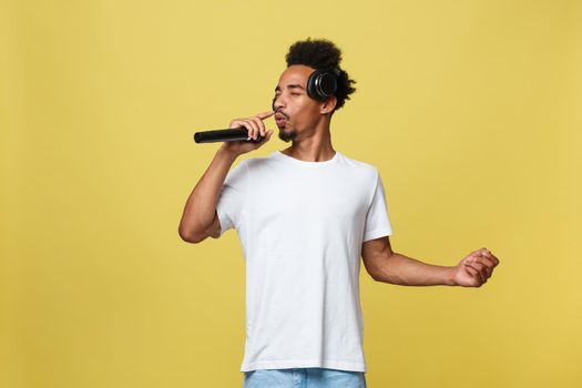 Young handsome African American Male Singer Performing with Microphone. Isolated over yellow gold background