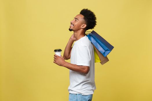 Handsome African American with shopping bag and take away coffee cup. Isolated over yellow gold background