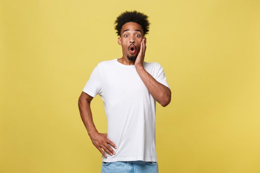 Advertising concept. Portrait of handsome African entrepreneur or office worker wearing suit pointing his finger at yellow studio wall with copy space for your content, looking shocked and surprised