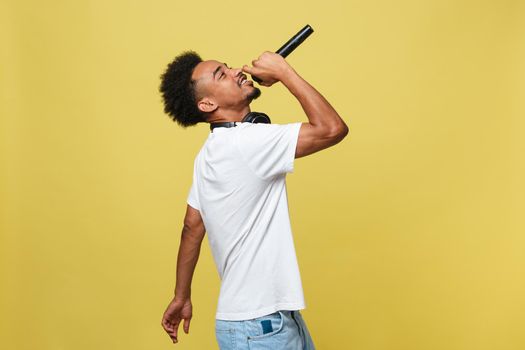 Young handsome African American Male Singer Performing with Microphone. Isolated over yellow gold background