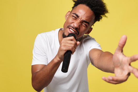 Stylish afro american man singing into microphone isolated on a yellow gold background.