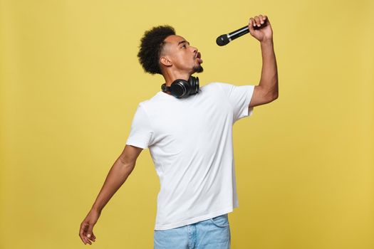 Young handsome African American Male Singer Performing with Microphone. Isolated over yellow gold background