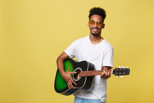 Happy african american musician man posing with a guitar, over golden yellow background