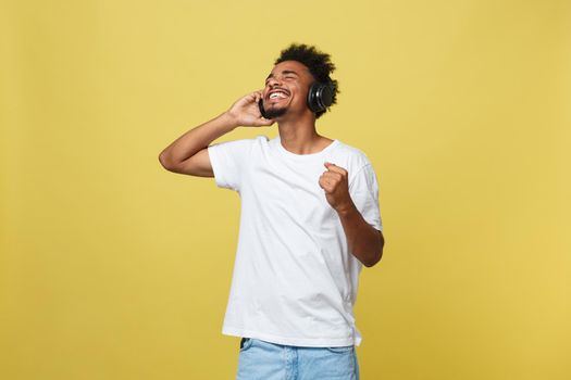 Young African American man wearing headphone and enjoy music over yellow gold Background.