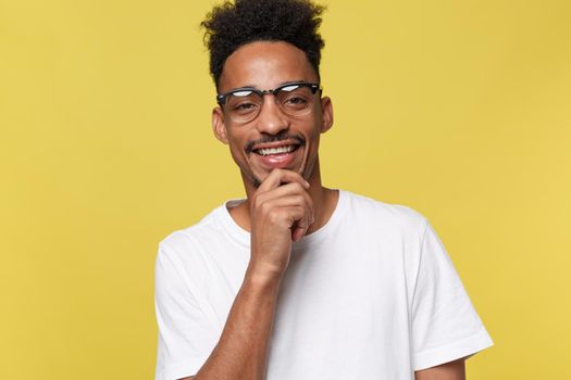 Headshot of good-looking positive young dark-skinned male with stubble and trendy haircut wearing white shirt while posing isolated against blank studio wall background with copy space for your text.