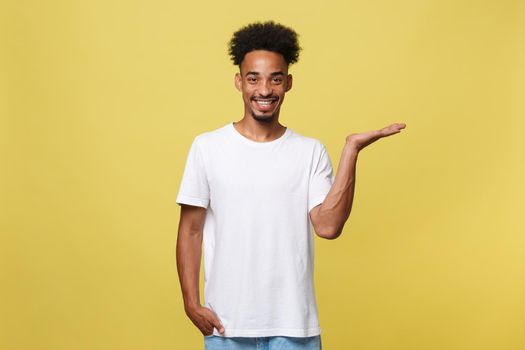 Charming handsome young black man holding his hand up to show present sell product. Isolated over yellow background