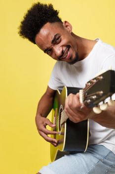 african american retro styled guitarist playing acoustic guitar isolated on yellow gold background.