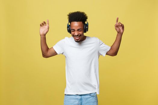 Young African American man wearing headphone and enjoy music over yellow gold Background.