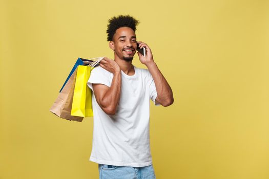 young man with shopping bags talking on smart phone isolated on yellow background.