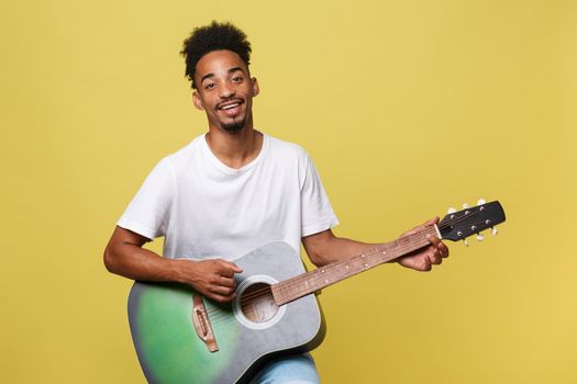 Happy african american musician man posing with a guitar, over golden yellow background