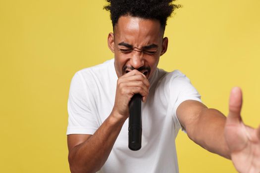 Stylish afro american man singing into microphone isolated on a yellow gold background.