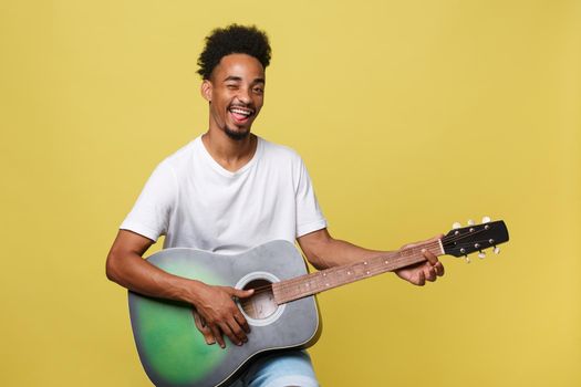 Happy african american musician man posing with a guitar, over golden yellow background