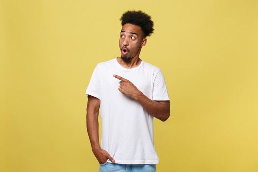 Indoor photo of young African American man pictured isolated on grey background pointing to his white blank T-shirt drawing attention to advertisement on it, promoting goods, apps or services