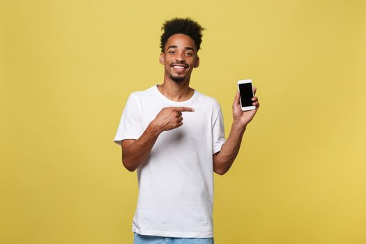 Portrait of attractive young black man isolated on yellow background, holding blank smartphone, smiling at camera, showing thubms up gesture, feeling happy