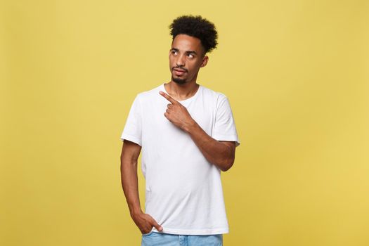 Indoor photo of young African American man pictured isolated on grey background pointing to his white blank T-shirt drawing attention to advertisement on it, promoting goods, apps or services