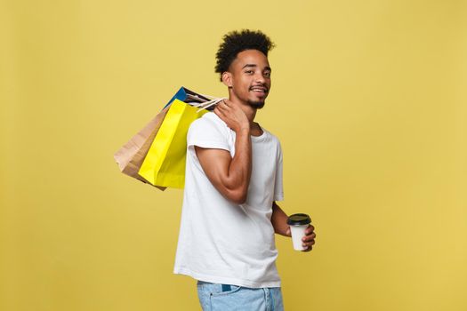 Handsome African American with shopping bag and take away coffee cup. Isolated over yellow gold background