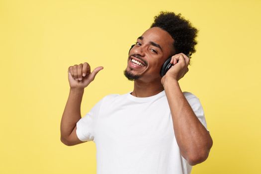 Attractive African American man with headphones listen to music. Isolated over yellow gold background