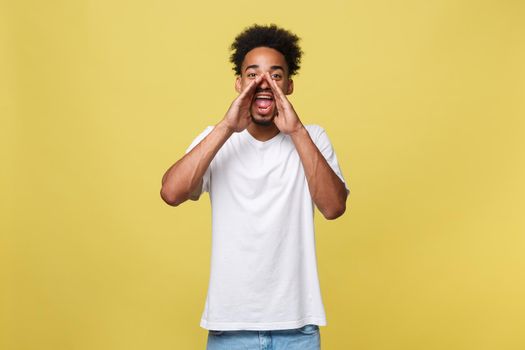 positive young black guy, student, worker employee screams mouth wide open and putting his hands to his face as mouthpiece. Portrait on white background in casual clothing