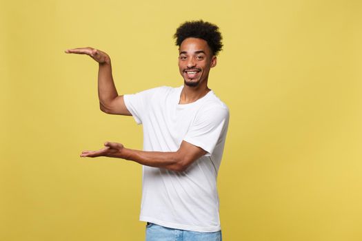 Charming handsome young black man holding his hand up to show present sell product. Isolated over yellow background