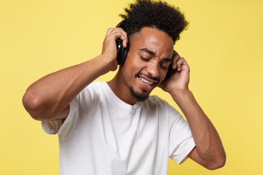 Attractive African American man with headphones listen to music. Isolated over yellow gold background