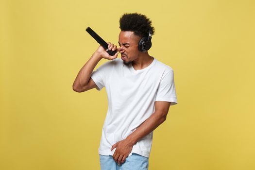 Attractive young dark-skinned man with afro haircut in white t shirt, gesticulating with hands and microphone, dancing and singing on party, having fun
