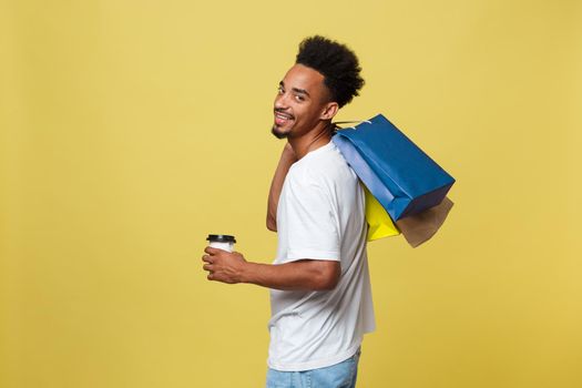 African American man with colorful paper bags isolated on yellow background.