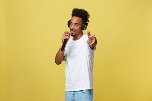 Young handsome African American Male Singer Performing with Microphone. Isolated over yellow gold background