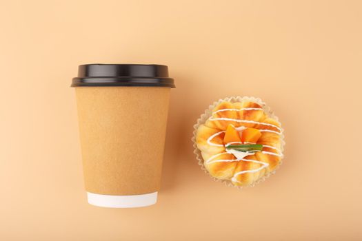 Top view of coffee or tea in brown cardboard cup with pastry against beige background. Concept of hot drinks, take away food, small breaks or cheat meal