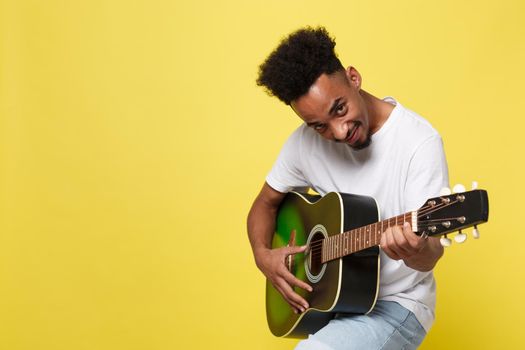 african american retro styled guitarist playing acoustic guitar isolated on yellow gold background.