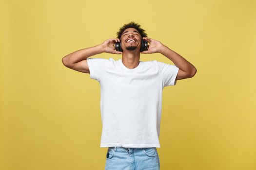 Young African American man wearing headphone and enjoy music over yellow gold Background.