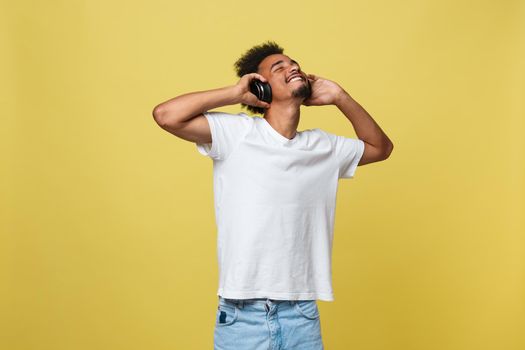 Young African American man wearing headphone and enjoy music over yellow gold Background.