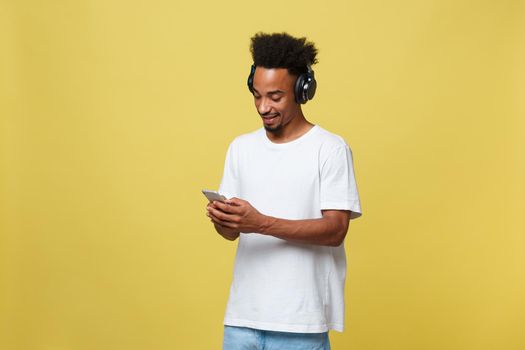 Young black man listening to music over his headphones. Isolated over yellow background