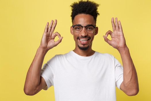 Portrait of happy african-american man showing ok sign and smiling, over yellow background.