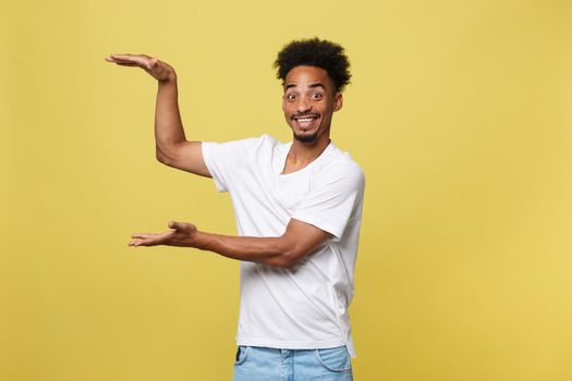 Charming handsome young black man holding his hand up to show present sell product. Isolated over yellow background