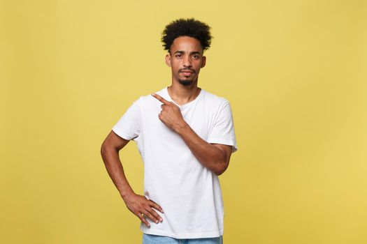 Indoor photo of young African American man pictured isolated on grey background pointing to his white blank T-shirt drawing attention to advertisement on it, promoting goods, apps or services