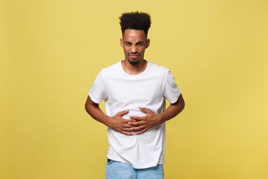 Closeup portrait of miserable, upset, young man, doubling over in stomach pain, looking very sick unwell, isolated on yellow background. Facial expressions emotion feelings, health issues.