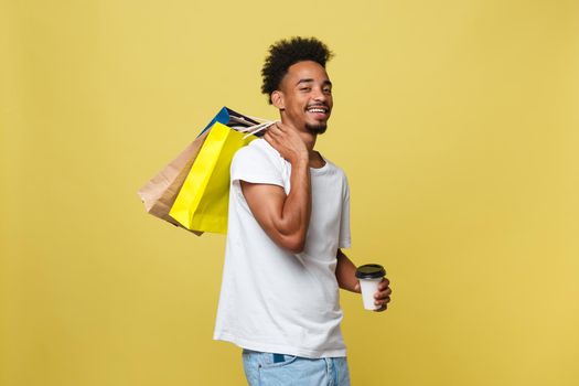 Handsome African American with shopping bag and take away coffee cup. Isolated over yellow gold background