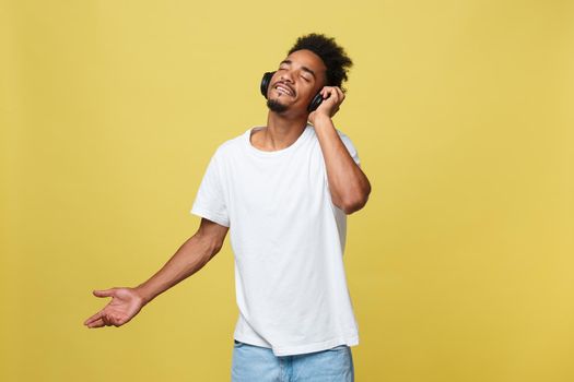 Young black man listening to music over his headphones. Isolated over yellow background