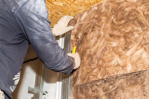 The worker attaches mineral wool to the walls for further plasterboard cladding. Thermal insulation and sound insulation of housing. Home renovation.
