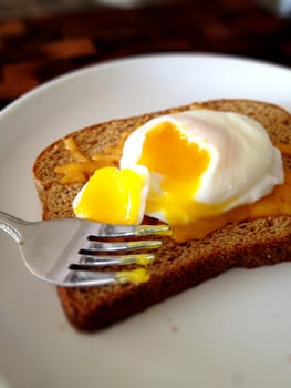 Image of Poached egg with yolk broken onto toast on a white plate against a dark background