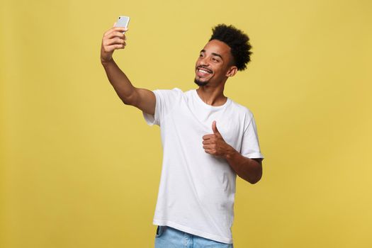 young afro american black man smiling happy taking selfie self portrait picture with mobile phone looking excited having fun posing cool isolated in yellow background in communication technology.