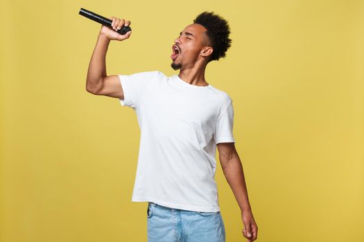 Young handsome African American Male Singer Performing with Microphone. Isolated over yellow gold background