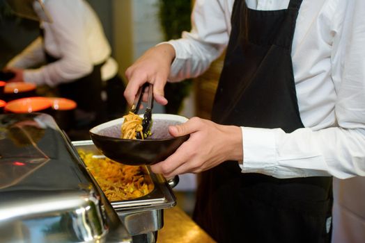 Black bowl with noodles served at a party by a waiter with a black kitchen apron