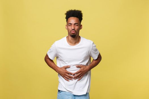 Closeup portrait of miserable, upset, young man, doubling over in stomach pain, looking very sick unwell, isolated on yellow background. Facial expressions emotion feelings, health issues.