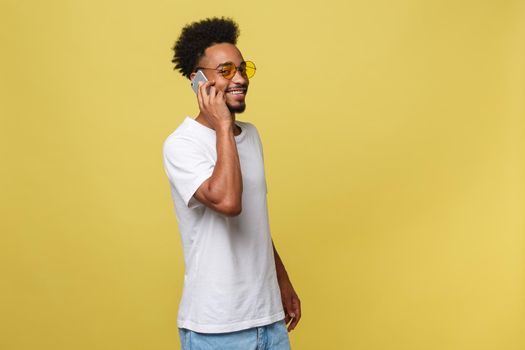 Portrait of cool young black guy talking on cellphone. Isolated on yellow background.