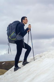 The traveler is engaged in extreme sports, climbs to the top of a snow-covered mountain with tourist equipment in backpacks and trekking poles. A young man is hiking alone in the winter wild nature.