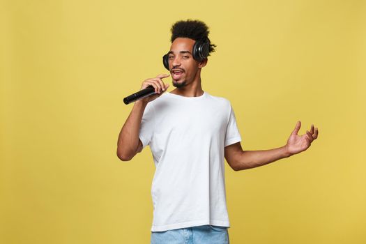 Attractive young dark-skinned man with afro haircut in white t shirt, gesticulating with hands and microphone, dancing and singing on party, having fun