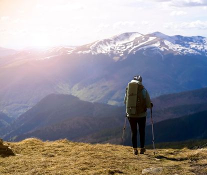 Young female travelers walk the trail on the mountainside, girls with backpacks go hiking in the national park in winter, a stunning view of the mountains in the snow at sunset on the background.