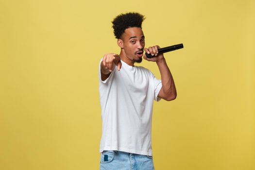 Attractive young dark-skinned man with afro haircut in white t shirt, gesticulating with hands and microphone, dancing and singing on party, having fun