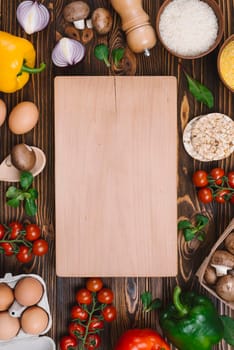 chopping board surrounded with vegetables eggs rice grains desk. High resolution photo
